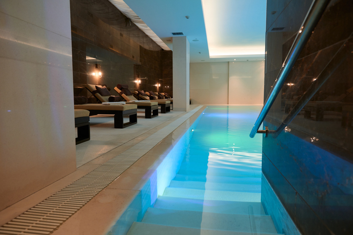 View of the modern luxurious interior of the spa and wellness center with sun loungers by the thermal pool with underwater lighting and a waterfall.